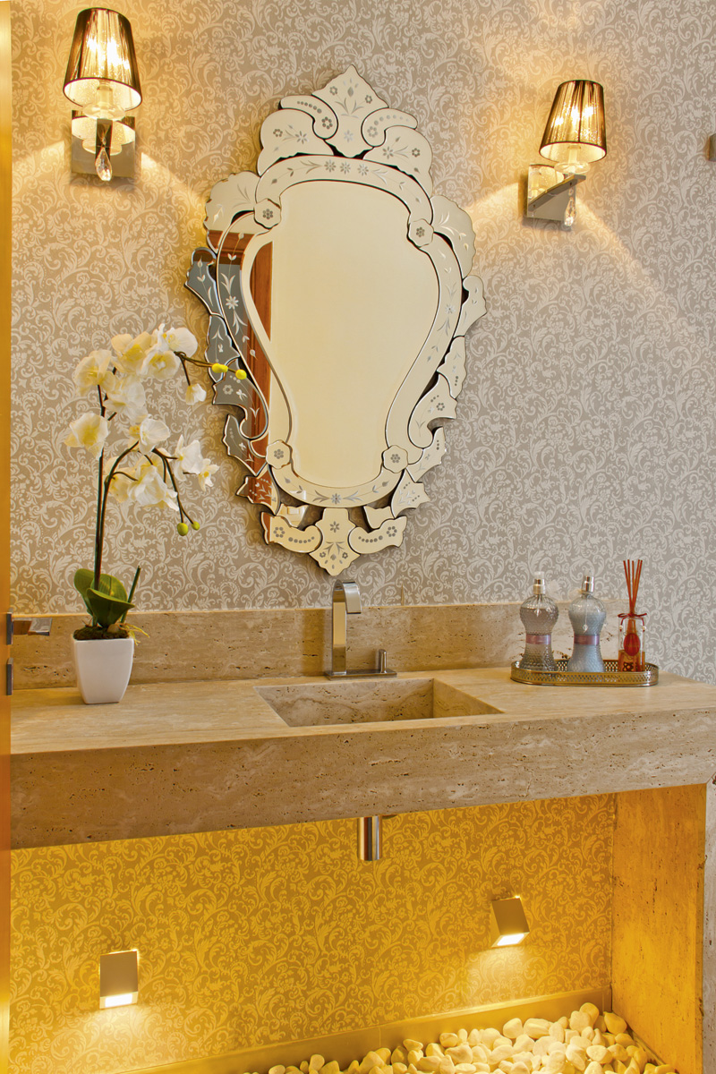 Sofisticado lavabo apresenta bancada em mármore Travertino Romano Bruto e papel de parede de arabescos