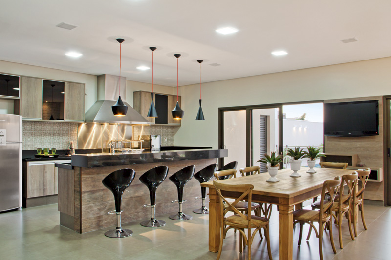 A área gourmet, ao lado, inspira contemporaneidade com o mobiliário planejado e bancada em granito preto São Gabriel