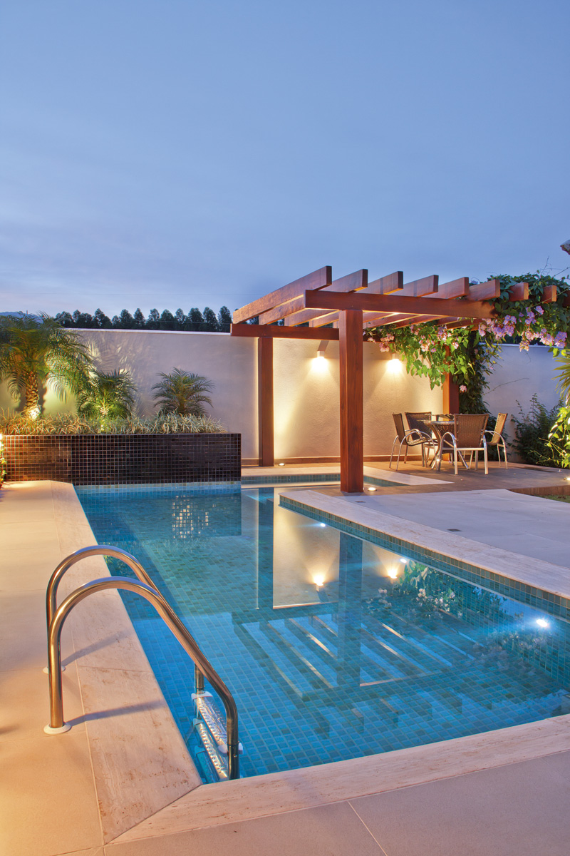 Piscina com iluminação e hidromassagem se une ao pergolado de madeira em uma composição que é puro charme