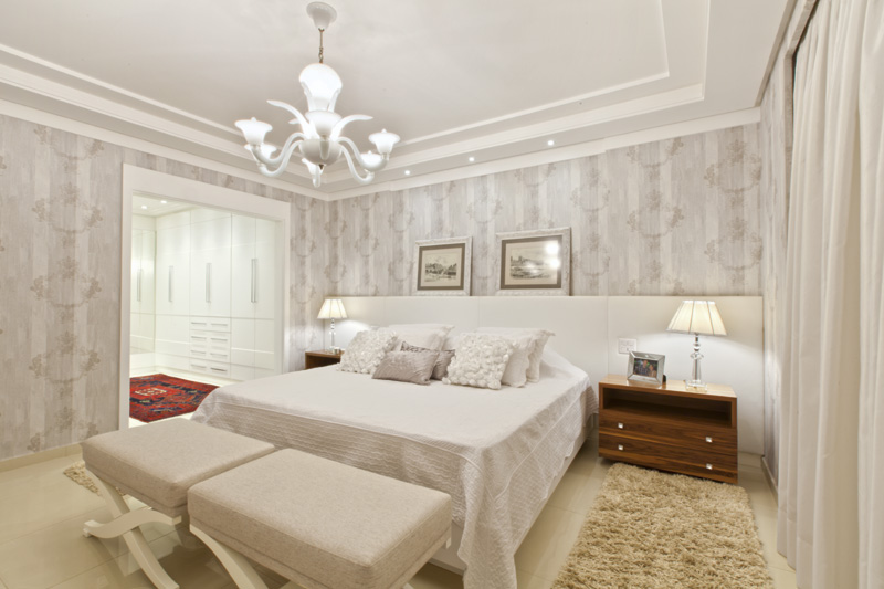 Único dormitório do segundo piso, a suíte master contempla o quarto, o closet, o banheiro e uma sacada privativa. A decoração romântica traz cabeceira de couro natural, armários brancos desenhados pela arquiteta, papel de parede, lustre italiano de Murano branco e abajures de cristal