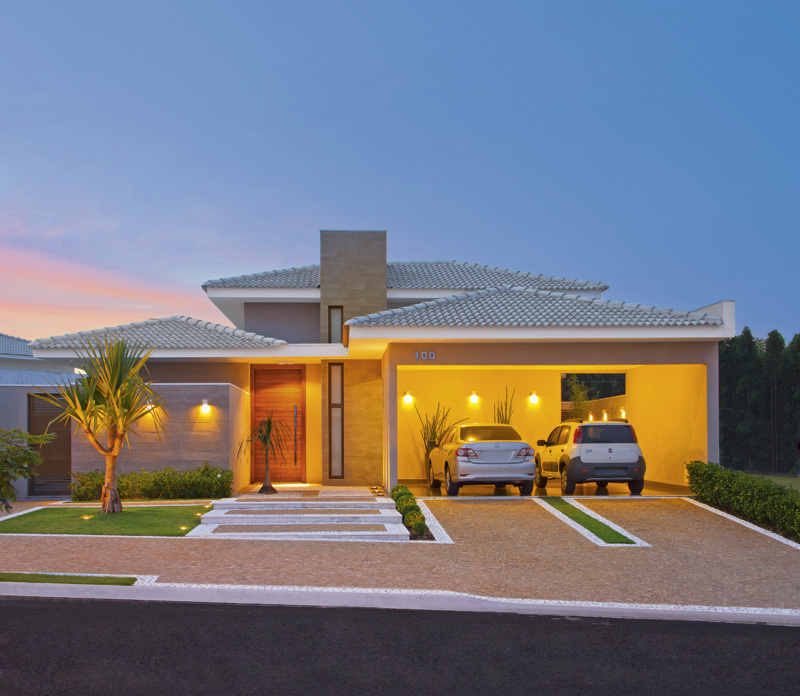 A fachada apresenta um belo projeto luminotécnico, com luzes pontuais que ressaltam as cores e formas do paisagismo. O porcelanato padrão concreto reveste as paredes. No piso, petit-pavet caramelo e branco