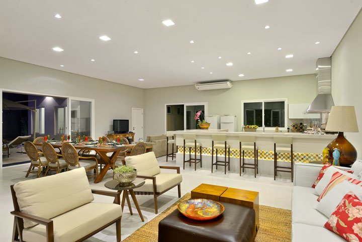 A área gourmet é completa, com mesa para almoços e um estar. Os móveis são da Aimar Móveis e da Mobiliarium Home e a coifa, na área da churrasqueira, é da Coifas e Coifas. Armários planejados da Kitchens.