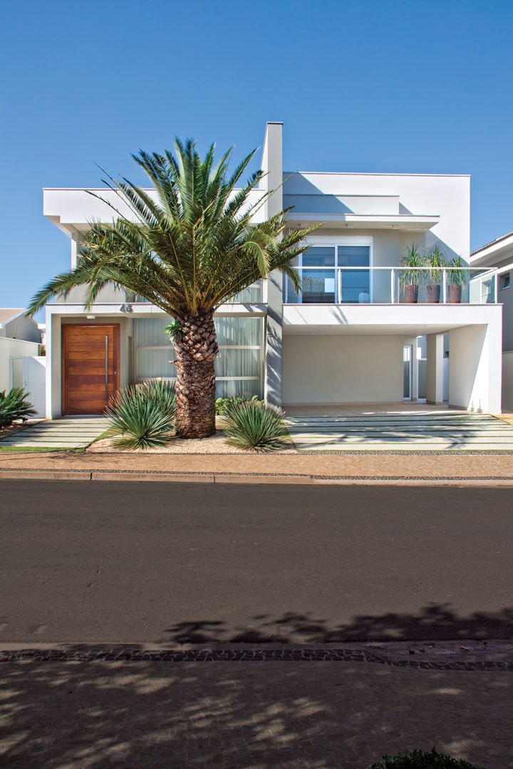 As linhas retas da residência ganharam leveza com o paisagismo executado pela Garden Cerri e com a abertura em vidro curvo (Box & Box). Uma generosa porta de entrada em madeira natural (Dara Portas) dá as boas-vindas. 