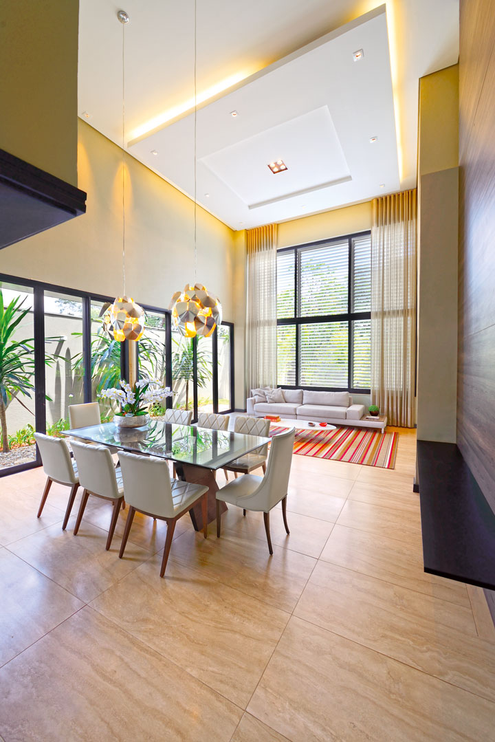 Living e jantar dividem o mesmo espaço com pé-direito duplo e jardins integrados por portas de vidro e alumínio preto (Alumimaster). O sofá do estar é da Mobiliarium Home e as cadeiras do jantar são da Sierra Móveis. Toda a iluminação é da Ilumax 