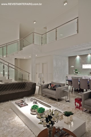 O mesmo mármore foi utilizado nos degraus da escada com corrimão em inox e vidro. O piso em porcelanato off White com brilho forma a base para os móveis de medidas generosas, como os sofás cinza em veludo e capitonê, as duas poltronas em shantung de seda prata e o tapete branco em seda de bambu. Sob o mezanino, o jantar traz mesa azul, luminária pendente e papel de parede grego com minerais (mica) incrustrados (Ateliê Revestimentos). As cadeiras em linho cinza e capitonê fazem o link com o living. 