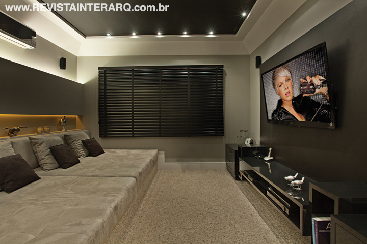 A iluminação indireta âmbar dá um toque dramático ao ambiente de cores escuras. O conforto dos moradores é garantido pelo grande futon sobre um tablado de madeira e o carpete. Para acomodar a TV e os equipamentos, os arquitetos projetaram um painel e um rack suspenso.