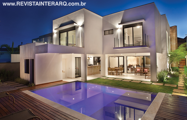 A piscina revestida com pastilhas cerâmicas foi elevada 60 cm em relação ao piso, o que permitiu criar pequenas quedas d’água nas bordas em mármore branco voltadas para o social e espaço gourmet, ambientado com poltronas de madeira 