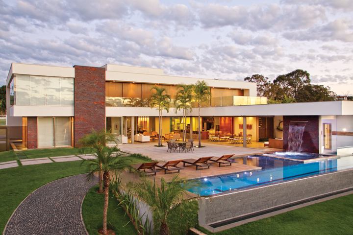 A piscina com raia, borda infinita, cascata e sauna flutuante é a protagonista da área de lazer, integrada ao social. Os móveis externos são da Pátio Brasil (Quadra Design). No segundo piso, o guarda-corpo de vidro revela a beleza das portas com brises deslizantes