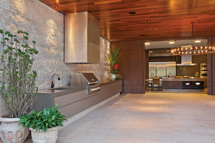 A parede em Travertino Antique da Palimanan (Vallori) acompanha toda a bancada em Silestone da área gourmet, com piso em Limestone Crema Europa 