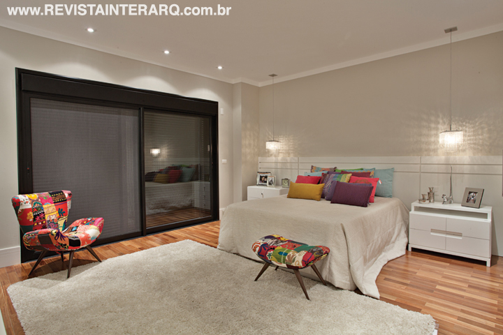 No pavimento superior ficam as quatro suítes interligadas pela passarela. No dormitório do casal, a base clean com móveis planejados brancos e tapete cinza faz contraponto às almofadas e banqueta de cores vibrantes 