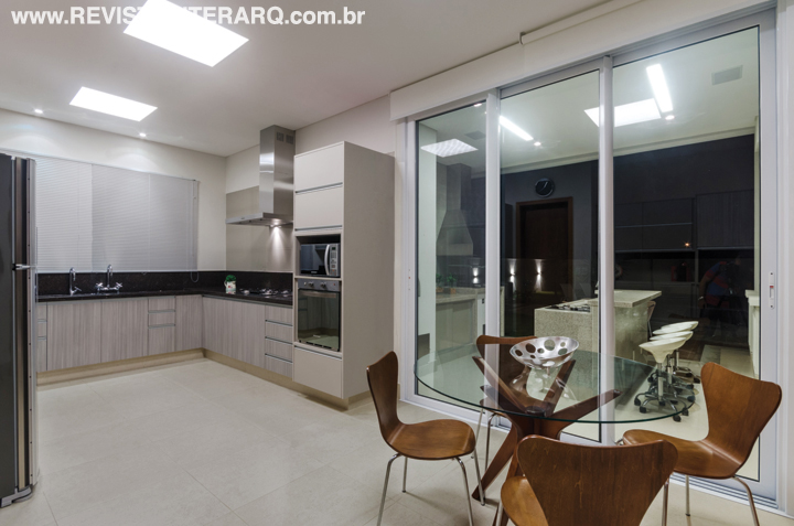 Portas de vidro integram a cozinha planejada com a área da churrasqueira. Coifa e cooktop da Máxima Coifas e revestimentos da Portobello Shop