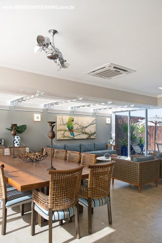 A varanda gourmet foi fechada e climatizada e transformou-se em um gostoso loft com móveis de madeira e fibra da Artenal. Na área do pergolado de vidro, a luz natural é filtrada por persianas de teto da Nice Decorações. Os acessórios decorativos são da Krieê