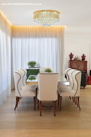 Cortinas em shantung de seda suavizam a luz natural que invade o jantar, com mesa e poltronas da Sierra Perfil Casa sob o lustre de cristais (NR Iluminação). O piso é em porcelanato da Portobello Shop