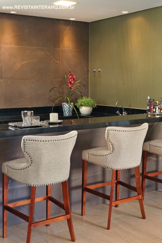 A bancada da cozinha gourmet foi revestida com porcelanato Bronze Armani (Portobello Shop) e granito Preto Absoluto. As banquetas da Visual Q agregam sofisticação ao espaço