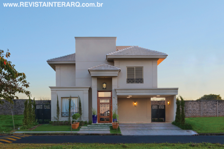 O paisagismo com ciprestes (Plant Garden) acompanha a atmosfera clássica da arquitetura com molduras e pórtico arrematando a porta de entrada em madeira e vidro. Gradis trabalhados (Quality Inox) e luminárias de estilo (NR Iluminação) finalizam a proposta