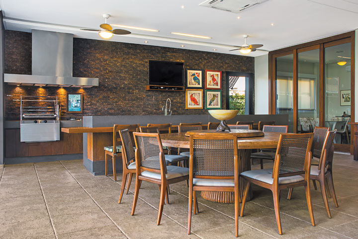 Ambientada com mesa de madeira de demolição (Depósito Kasa) e cadeiras com telinha (Decorativa). Na área da churrasqueira, a personalidade contemporânea foi acentuada pela bancada em Caesarstone (Stone Center), tijolos de demolição e coifa em inox (Refrigeração Araçatuba). O piso em porcelanato ShellStone é da Ornamentare