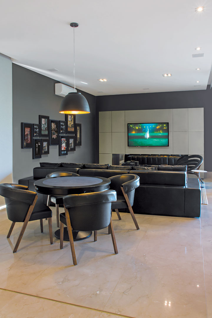 A mesa de jogos sob a luminária preta (ViaLight) ocupa o mesmo cenário que o home theater com paredes mais escuras. Os móveis são da Decorativa