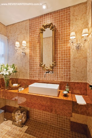 O lavabo ganhou revestimentos nobres de apelo clássico, mas com linguagem contemporânea, como o mármore Roso Verona em forma de pastilhas, na parede e no piso (Casa dos Construtores), e polido, na bancada (Marmoraria Lapidare). Arandelas de cristal (Casa Luz) compõem com o espelho com folhas de ouro (P.O. Móveis e Estofados). Louças e metais da Casa dos Construtores