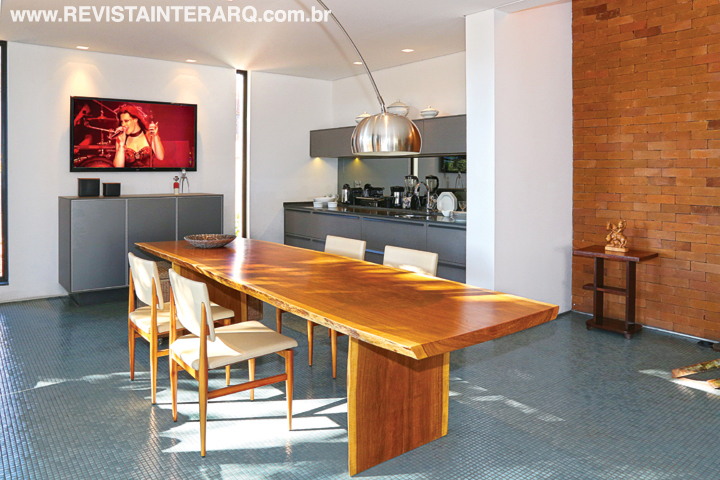 A cozinha tipo gourmet teve todos os equipamentos “camuflados” pela marcenaria em tom cinza, que compõe com a bancada em Silestone. O backsplash com espelho fumê dá profundidade ao ambiente e o cooktop de indução móvel permite o uso na bancada ou na mesa de jantar