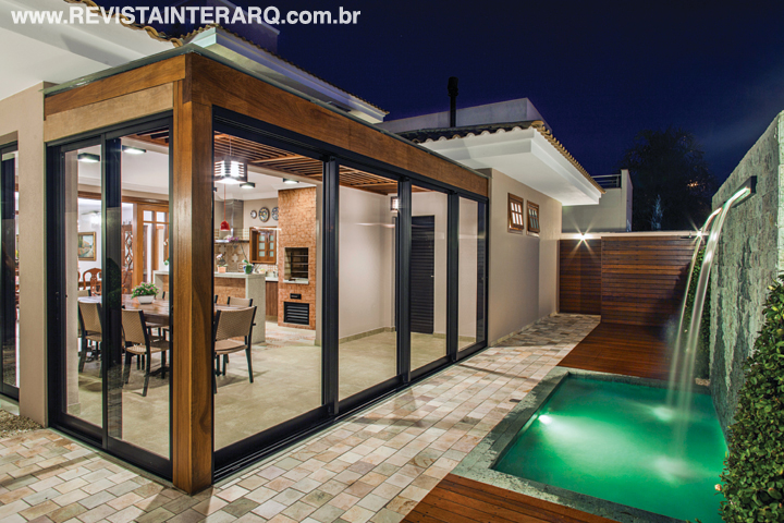 Portas de correr em alumínio e vidro (RN Aluminiun) convidam os jardins e a piscina com cascata (Casa das Bombas) a participar das reuniões festivas. Coifa da Máxima Coifas, metais da Jabu e pedras externas da MM Pedras