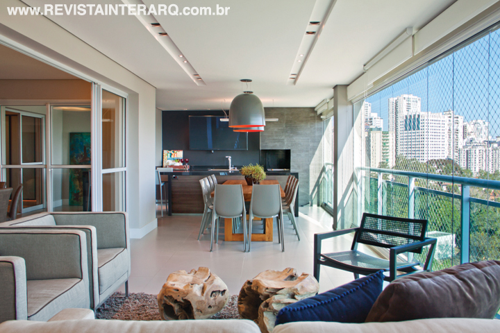 Para favorecer a unidade visual, o espaço gourmet foi revestido com porcelanato da Portobello Shop, mesmo piso do social. Persianas rolô Hunter Douglas (Villa Cores) suavizam a luz natural e acentuam o clima receptivo do espaço com mesa, cadeiras e poltronas da Casa Decorada