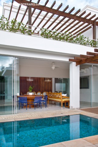 Piscina, pérgolas de madeira e varanda decorada com bancada em Marmoglass branco, cadeiras e banquetas azuis