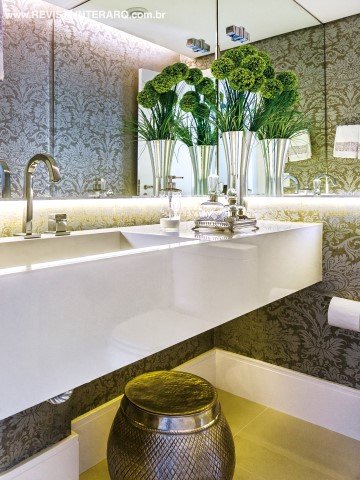 No lavabo, destaque para a iluminação embutida no espelho, valorizando o papel de parede da Orlean. À direira, no living, os móveis se destacam pela elegante paleta neutra, com preto, cinza e off-white. O tapete estampado da Santa Mônica confere dinamismo ao décor (tudo da Firmato Móveis)