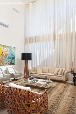 Para acompanhar a base neutra, cortinas de linho claro (Nice Decorações) “vestem” toda a altura dos vãos de vidro do living. O sofá e as poltronas (tudo da Aparato) seguem a mesma proposta clean, “aquecida” pelo tapete em zigue-zague (Decorativa) e luminária de piso em madeira (Jackie). A tela colorida é uma foto do casal transformada em arte