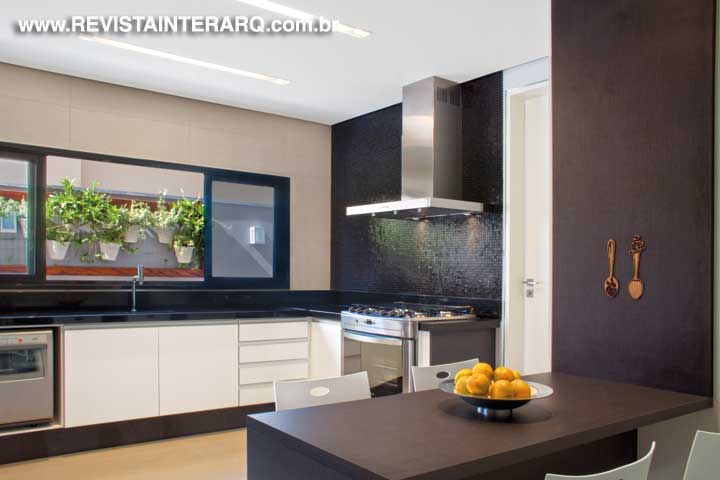 A cozinha tem acesso direto ao espaço gourmet/varanda, projetada na parte frontal da residência. Os móveis modulados ganharam a companhia das cadeiras em polipropileno e da cortina rolô em tela solar Panamá, da Hunter Douglas