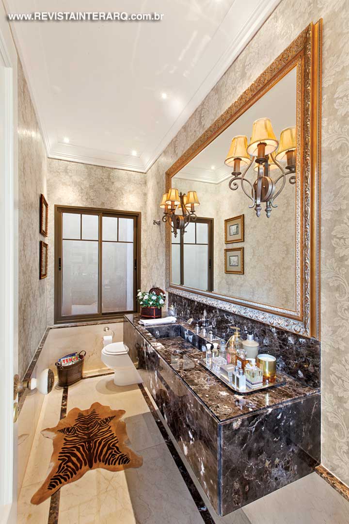 No lavabo, o espelho com moldura dourada acompanha toda a bancada em mármore Marrom Imperial