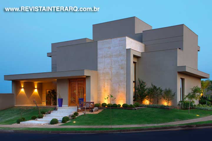 A fachada exibe um generoso painel em mármore Travertino Romano Bruto destacado pelas luzes pontuais (ViaLight). A porta em madeira com venezianas permite controlar a luz e a ventilação na entrada da casa