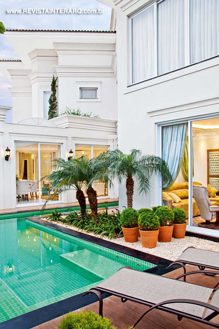 A piscina revestida com pastilhas verdes acompanha toda a lateral até o interior da casa. A borda em quartzo negro Stellar delimita também o deck, revestido com porcelanato Ecowood da Portobello Shop