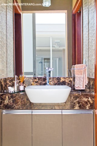 O lavabo funciona também como vestiário da piscina e foi fechado com portas de correr com vidro jateado (Aluart). Nas paredes, o mosaico marchetaria (Portobello Shop) compõe com a bancada em granito Marrom Imperial (Lola Mármores e Granitos) e com os armários na cor cobre Metalic (Ferrari Marcenaria). O piso do lavabo e do gourmet são em porcelanato acetinado da Portinari (Casa dos Construtores)