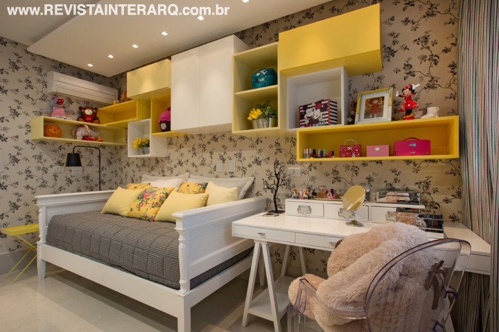 A marcenaria assimétrica com nuances de amarelo, executada pela Móveis RM, confere movimento ao dormitório da menina, que tem base preta e branca. O papel de parede floral e o enxoval são da Délicatesse Tecidos. Luminária de piso da Kelvin LD