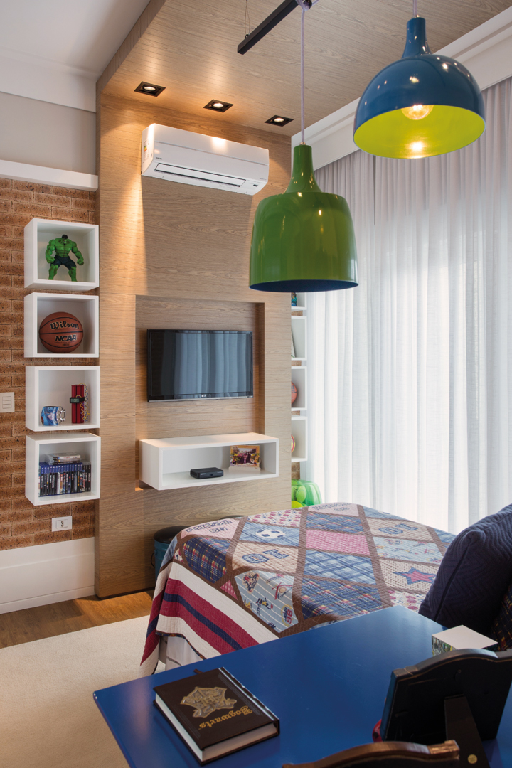 Para o menino, o dormitório teve uma das paredes revestida com o despojamento do tijolo inglês. A marcenaria (Incomap Móveis) forma um “L” e acomoda a TV e brinquedos. Ar condicionado da Ambiente e iluminação da Kelvin LD