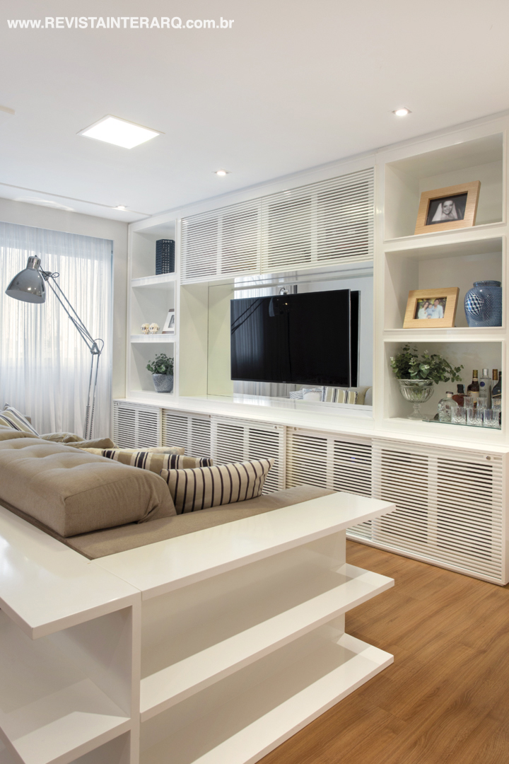 Detalhe da marcenaria em laca do home theater, executada pela Incomap Móveis. Um móvel “abraça” o sofá. Na estante, nicho espelhado e portas ripadas. TV da Digital Home e almofadas da Délicatesse Tecidos