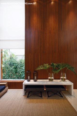 Um imenso painel em madeira acompanha o pé-direito duplo do hall de entrada, que se une ao verde do jardim lateral (Flora Decari) graças à janela em vidro com esquadria de PVC (Única PVC)