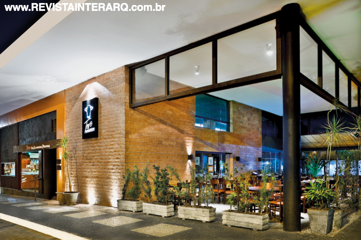 A fachada do restaurante tem a personalidade definida pela composição com tijolinho aparente, pintura alaranjada, chapa corten e malhas de vergalhão de obra. Detalhe da viga em concreto ressaltando a estrutura do prédio original, recoberta pela nova estrutura em ferro