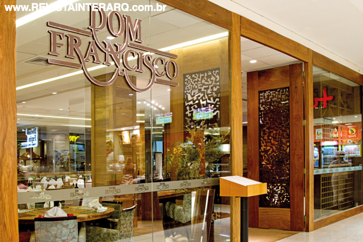 A porta de entrada do restaurante, com trabalho em chapa recortada de aço Corten, é uma verdadeira obra de arte executada pelo artista local Nemm Soares. Panos de vidro permitem visualizar o interior e destacam a logo da empresa