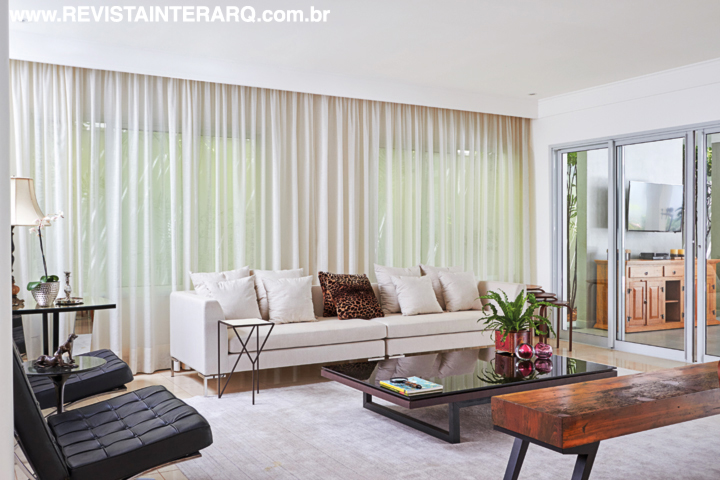 A leveza visual predomina no estar aberto à varanda. O tapete (By Kamy), sofá (Jackie Móveis) e cortinas revelam a eficácia do branco para acentuar a sensação de amplitude. Poltronas Barcelona e mesa de centro pretas fazem o contraponto. Banco em madeira de demolição da Perfil Casa e mesa lateral da Jackie Móveis
