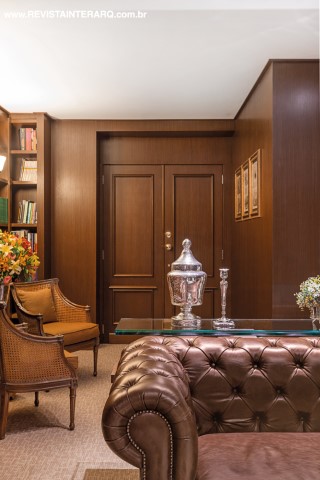 Na sala de espera, os sofás Chesterfield em couro marrom (Estofados Cardoso) se unem à marcenaria com boiseries e às poltronas clássicas (Perfil Casa) para remeter ao estilo inglês. Mesa de vidro da Perfil Casa e acessórios da Marizza Prado