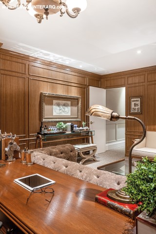 Os sofás Chesterfield em couro marrom (Estofados Cardoso) se unem à marcenaria com boiseries e às poltronas clássicas (Perfil Casa) para remeter ao estilo inglês. Mesa de vidro da Perfil Casa e acessórios da Marizza Prado