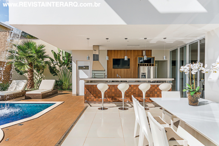 A bancada gourmet tem revestimento rústico em contraponto às modernas banquetas brancas. Entre o jardim e a piscina, chaises com estofados convidam a relaxar. 