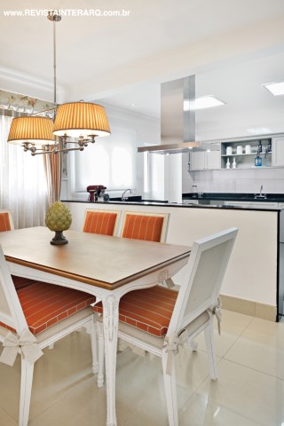 Na cozinha, o mobiliário da linha Charm, da Florense, acompanha a linguagem romântica da sala de almoço, com lambri de gesso, papel de parede floral (ACB Casa) e luminárias de estilo (Luminá Ribervent). Mesa e cadeiras da UneRobusti, bancada em granito preto da Marmoraria Exclusive e metais da Duo Deca