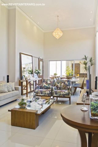 O living com grandes aberturas e pé-direito alto tem piso em porcelanato claro (Casa dos Construtores) e mobiliário moderno em madeira