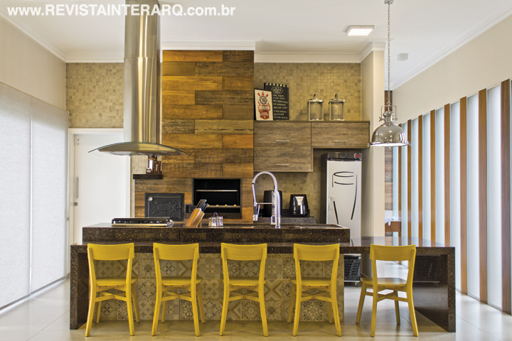 O lazer convida a longos happy hours, com cooktop, coifa, chopeira, churrasqueira e balcão refrigerado. Bancada em granito Marrom Café (Vidraçaria e Marmoraria Destak), patchwork de ladrilhos (Casa dos Construtores) e luminária tipo industrial da Casa Luz. Toda pintura é da Sotintas