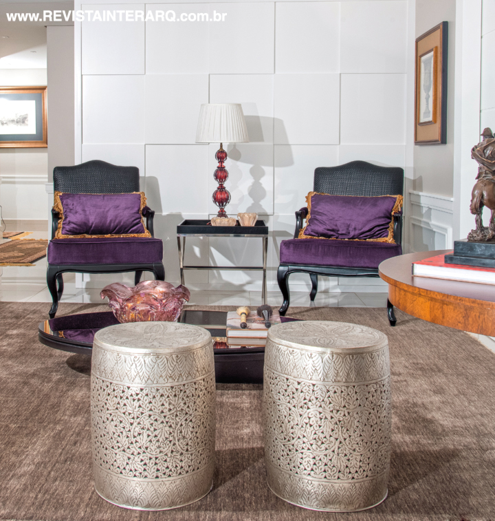 O toque de cor ficou por conta das poltronas em veludo roxo (UneRobusti). Garden seats em metal trabalhado (UneRobusti) e a parede com revestimento geométrico evocam o luxo