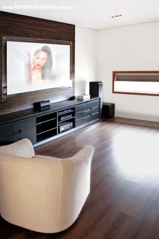 No home theater, o destaque é o móvel em laca preta em contraponto à poltrona em suede areia (Robusti)
