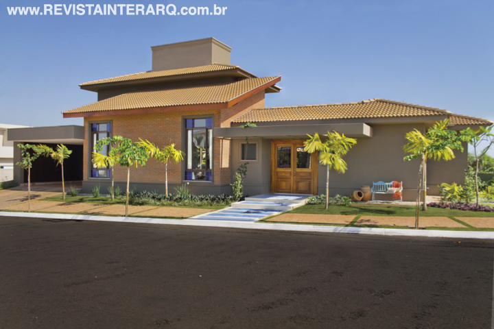 Tijolos de demolição (Pedregal), telhas cerâmicas, vitrais coloridos e jardins com palmeiras (Verdeplan) revelam a alma brasileira da fachada. A textura escura (Dantecolor) ressalta a porta de madeira de demolição e o canto com banco azul turquesa, mesma cor dos ladrilhos hidráulicos (CJÔ Revestimentos) nos degraus da entrada