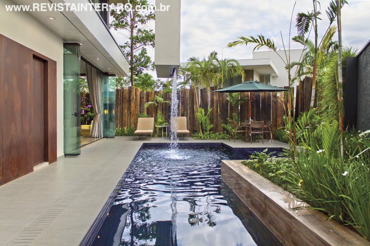 A cascata suspensa é uma das surpresas da área externa, com piscina revestida com pastilhas azul marinho e entorno em porcelanato (tudo da Portobello Shop). Móveis da Perfil Casa e painel em aço corten da Alupoli. Cortina de vidro que setoriza a varanda da Divettro